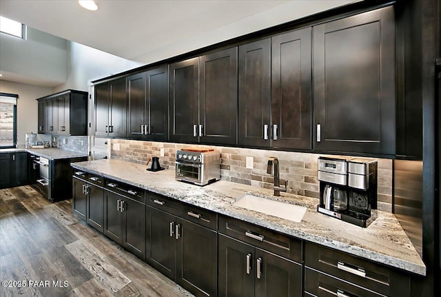kitchen with light stone counters, a sink, recessed lighting, tasteful backsplash, and dark wood-style floors