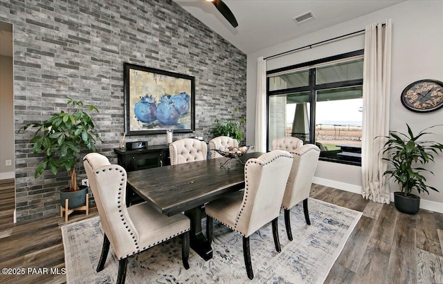dining area with baseboards, visible vents, wood finished floors, and brick wall