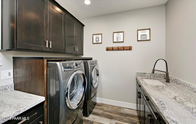 laundry area featuring cabinet space, a sink, baseboards, wood finished floors, and washing machine and dryer