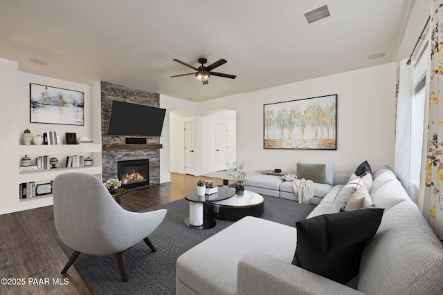living room with a fireplace, dark wood-style floors, visible vents, and ceiling fan
