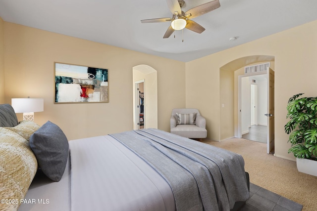 carpeted bedroom with arched walkways, baseboards, visible vents, and a ceiling fan