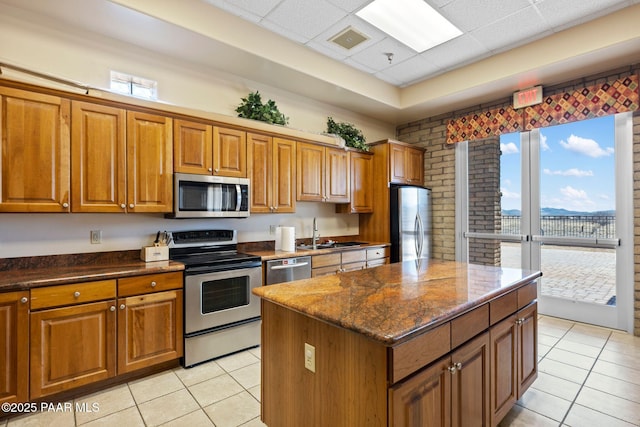 kitchen featuring light tile patterned floors, a sink, brown cabinets, and appliances with stainless steel finishes