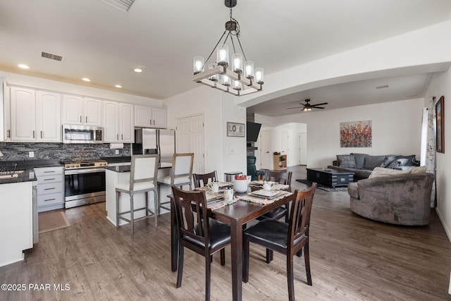 dining space with recessed lighting, ceiling fan with notable chandelier, arched walkways, dark wood-style floors, and visible vents