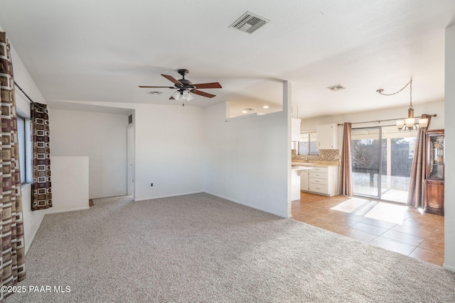 unfurnished living room featuring ceiling fan with notable chandelier, light tile patterned floors, light colored carpet, and visible vents