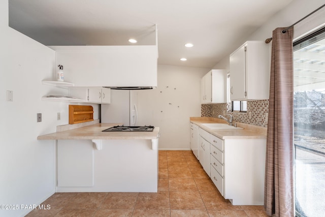 kitchen featuring a peninsula, freestanding refrigerator, a sink, decorative backsplash, and light countertops