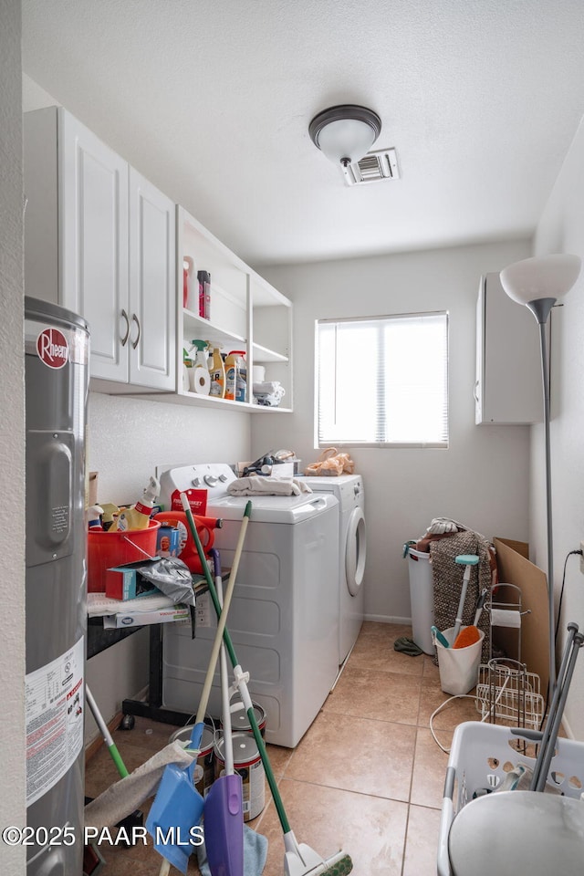 clothes washing area with visible vents, washer and clothes dryer, electric water heater, cabinet space, and light tile patterned floors