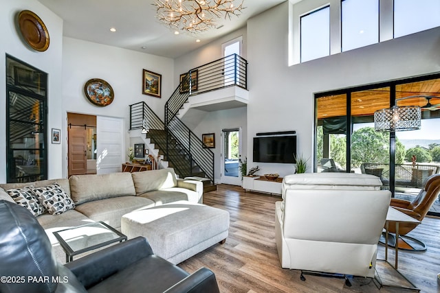 living room with a towering ceiling, wood-type flooring, a barn door, and an inviting chandelier