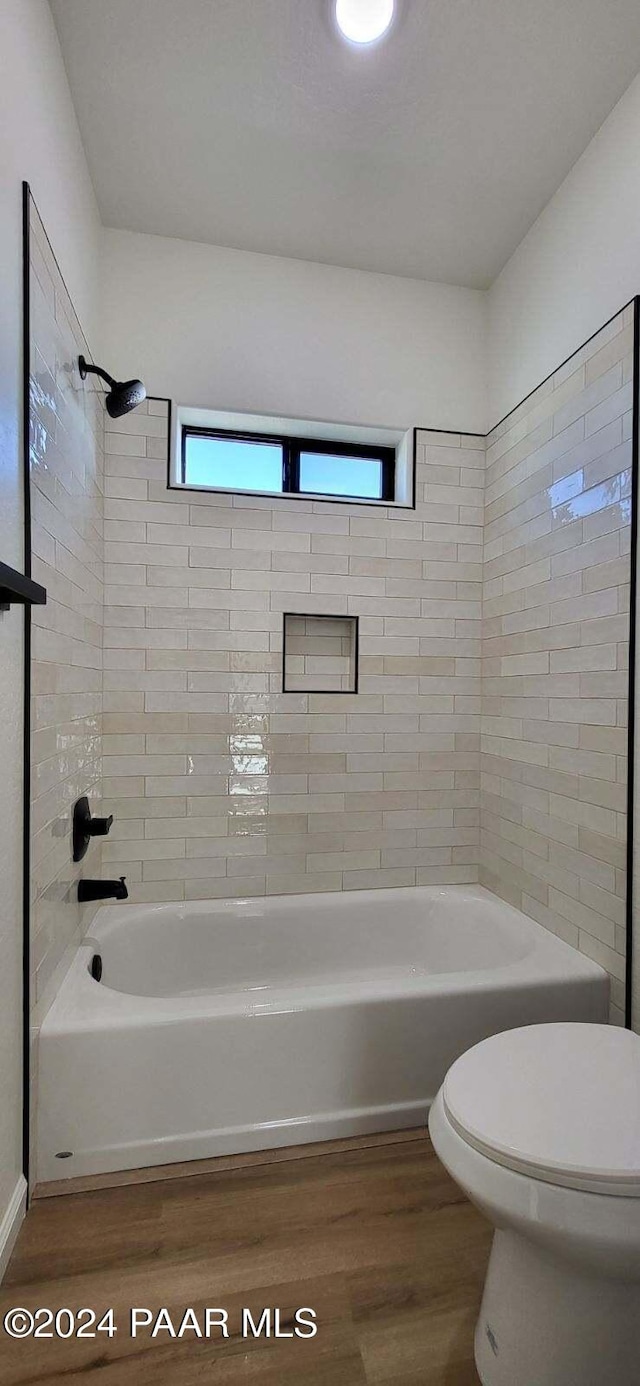 bathroom with hardwood / wood-style flooring, tiled shower / bath combo, and toilet