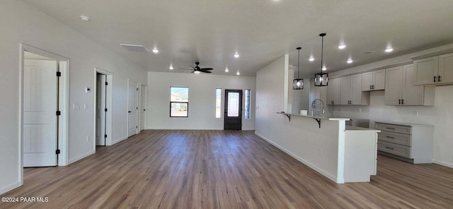 kitchen featuring ceiling fan, hanging light fixtures, kitchen peninsula, wood-type flooring, and a kitchen bar