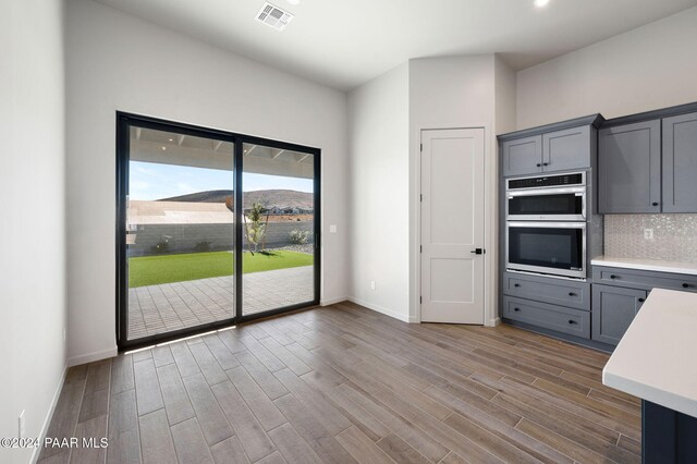 kitchen with tasteful backsplash, double oven, a mountain view, gray cabinets, and hardwood / wood-style flooring