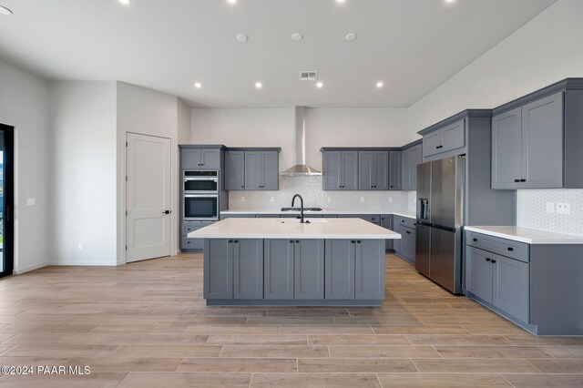 kitchen featuring gray cabinetry, a center island with sink, wall chimney range hood, and light wood-type flooring