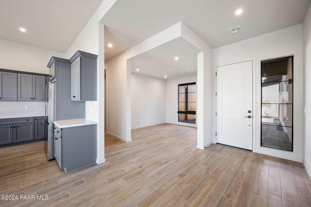 kitchen featuring light wood-type flooring, gray cabinets, stainless steel refrigerator, and tasteful backsplash