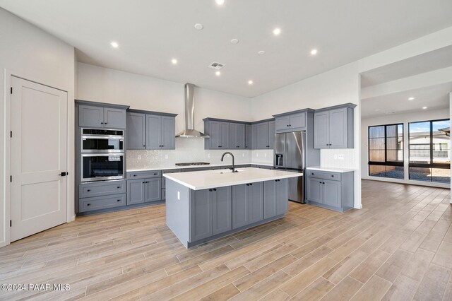 kitchen featuring gray cabinets, stainless steel appliances, light hardwood / wood-style flooring, and wall chimney exhaust hood