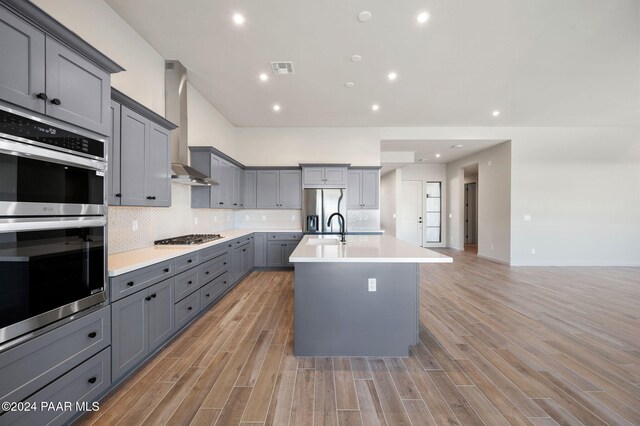 kitchen with gray cabinets, appliances with stainless steel finishes, wall chimney exhaust hood, and light wood-type flooring