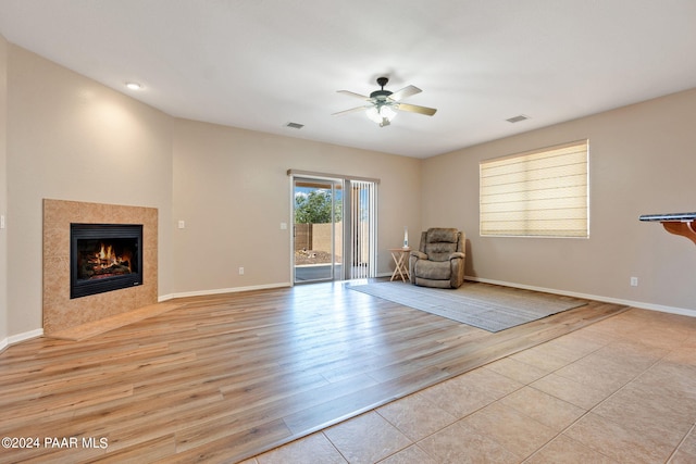 unfurnished room featuring light wood-type flooring, ceiling fan, and a tiled fireplace