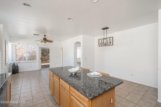 kitchen featuring light tile patterned floors, dark stone countertops, black dishwasher, a kitchen island, and pendant lighting