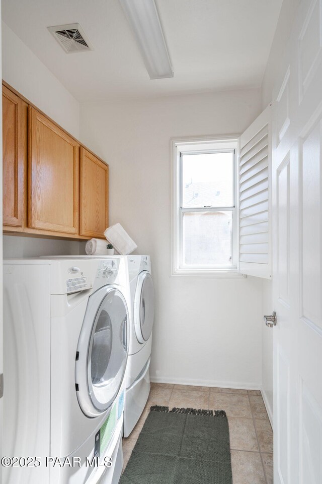 clothes washing area with cabinets, washing machine and clothes dryer, and light tile patterned flooring