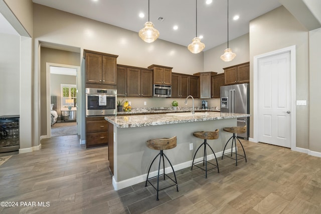 kitchen with a breakfast bar, stainless steel appliances, hanging light fixtures, and an island with sink