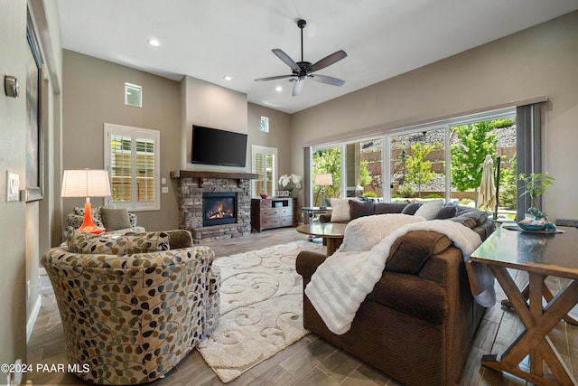 living room featuring ceiling fan, a stone fireplace, and wood-type flooring