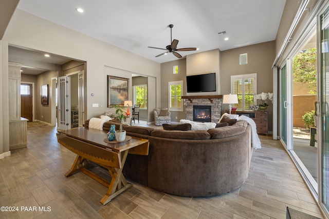 living room featuring a stone fireplace, ceiling fan, plenty of natural light, and light hardwood / wood-style floors