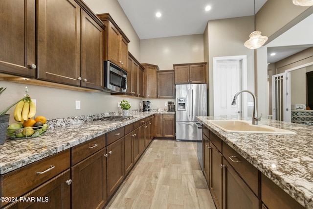 kitchen with light stone countertops, sink, pendant lighting, appliances with stainless steel finishes, and light wood-type flooring