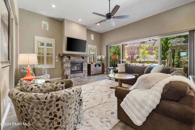 living room featuring ceiling fan, a stone fireplace, and light wood-type flooring