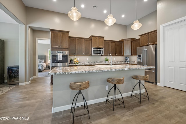 kitchen with a kitchen island with sink, sink, hanging light fixtures, a kitchen bar, and stainless steel appliances