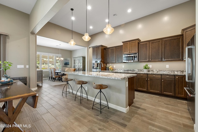 kitchen featuring a kitchen bar, light stone counters, stainless steel appliances, a kitchen island with sink, and pendant lighting