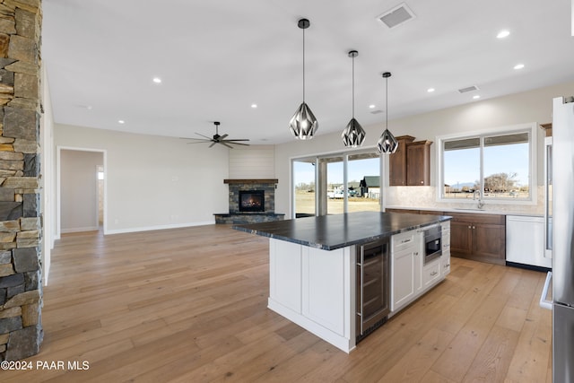 kitchen with a stone fireplace, wine cooler, light hardwood / wood-style flooring, appliances with stainless steel finishes, and white cabinetry