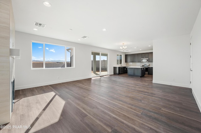 unfurnished living room featuring an inviting chandelier and dark wood-type flooring