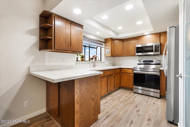 kitchen featuring brown cabinetry, a raised ceiling, appliances with stainless steel finishes, light wood-style floors, and open shelves