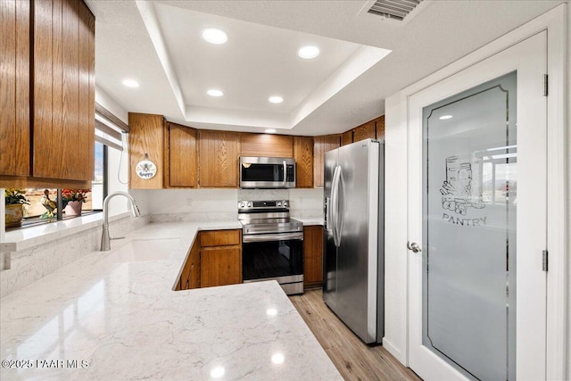 kitchen with a sink, visible vents, appliances with stainless steel finishes, brown cabinetry, and a raised ceiling