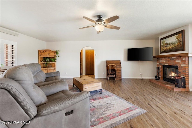 living room with arched walkways, a brick fireplace, baseboards, and light wood-style floors