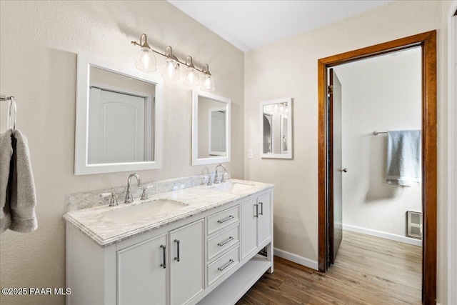 full bathroom with double vanity, baseboards, a sink, and wood finished floors