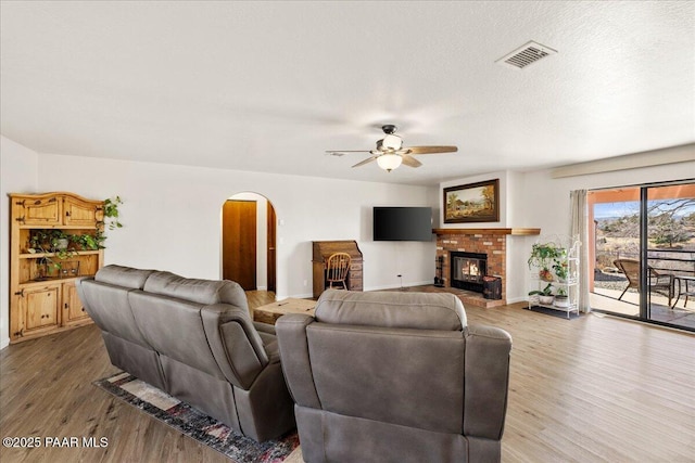 living area featuring arched walkways, a fireplace, visible vents, a textured ceiling, and wood finished floors