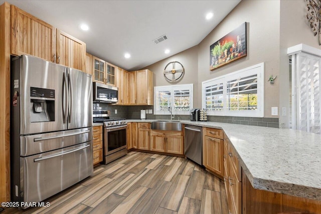 kitchen with sink, hardwood / wood-style flooring, appliances with stainless steel finishes, tasteful backsplash, and kitchen peninsula