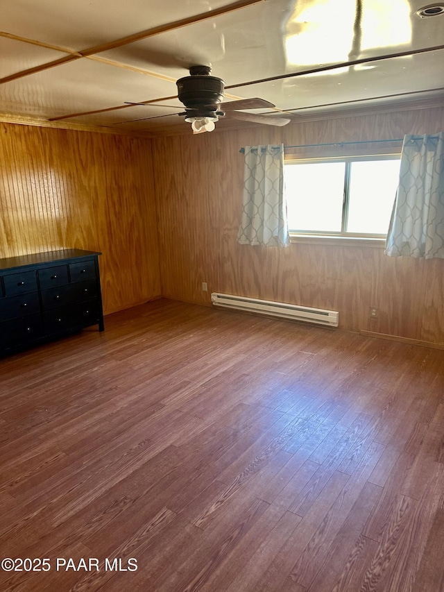 empty room featuring ceiling fan, wood walls, baseboard heating, and wood-type flooring