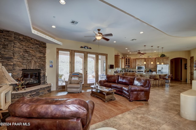 living area with a ceiling fan, arched walkways, a stone fireplace, light tile patterned flooring, and recessed lighting
