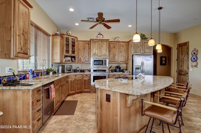 kitchen featuring stainless steel appliances, a ceiling fan, a kitchen breakfast bar, a kitchen island, and light stone counters