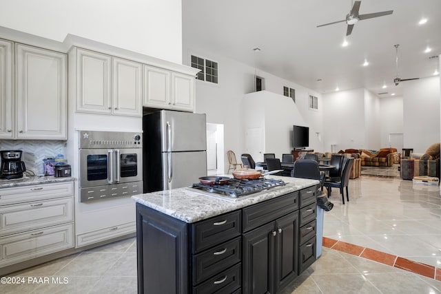 kitchen with white cabinetry, stainless steel appliances, a kitchen island, tasteful backsplash, and light tile patterned flooring