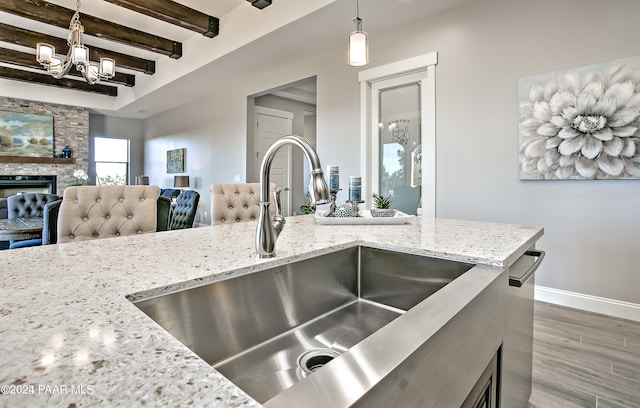 kitchen with a stone fireplace, sink, beamed ceiling, light stone counters, and pendant lighting