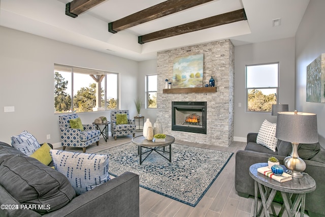 living room featuring beamed ceiling, a stone fireplace, and a wealth of natural light