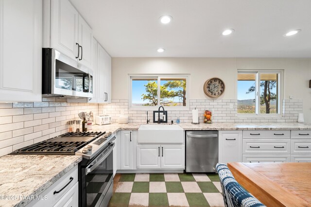 kitchen featuring a wealth of natural light, a sink, appliances with stainless steel finishes, white cabinets, and light floors