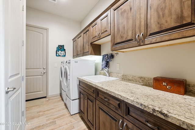 clothes washing area featuring washing machine and clothes dryer, visible vents, a sink, light wood-style floors, and cabinet space
