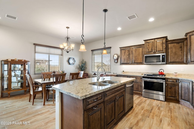 kitchen with light stone countertops, a sink, light wood-style flooring, a kitchen island with sink, and appliances with stainless steel finishes