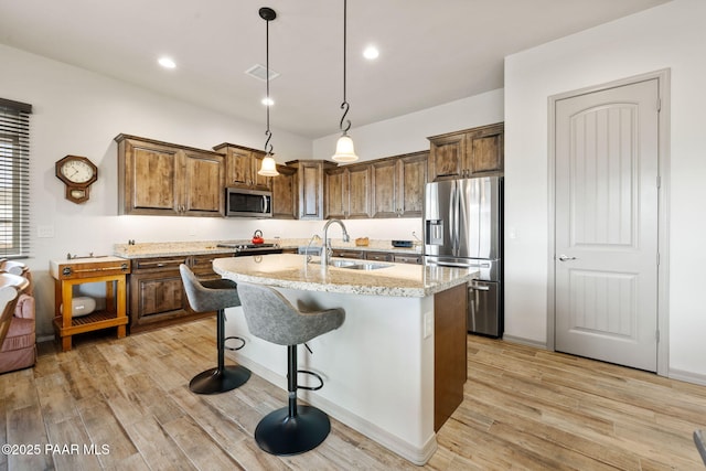 kitchen featuring an island with sink, a sink, stainless steel appliances, and light wood-type flooring