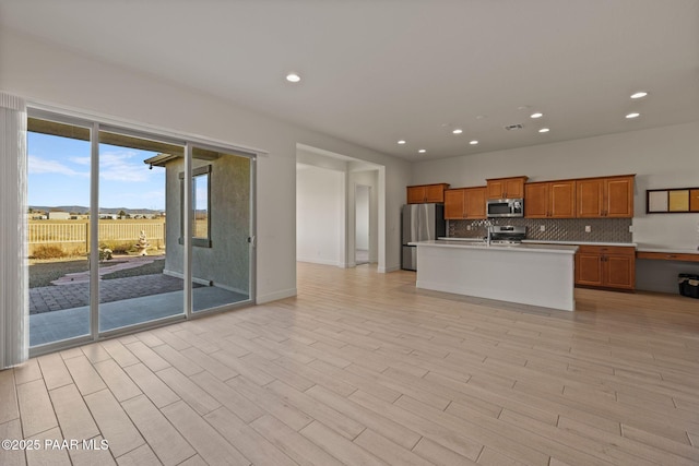 kitchen with stainless steel appliances, light countertops, backsplash, brown cabinetry, and open floor plan