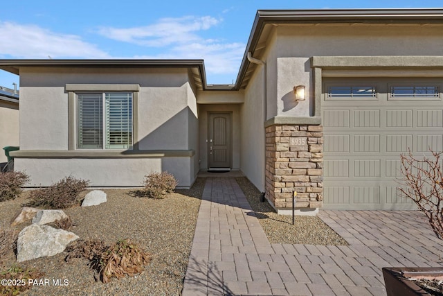 view of exterior entry featuring a garage, stone siding, and stucco siding