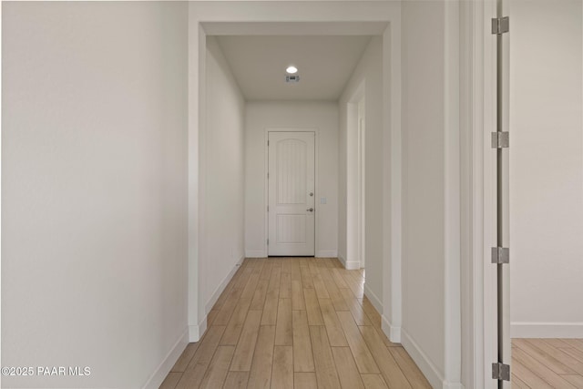 hallway with light wood finished floors, visible vents, and baseboards