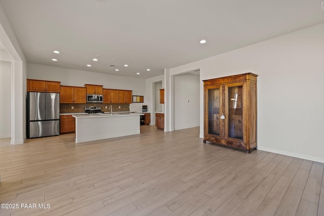 kitchen featuring sink, light wood-type flooring, stainless steel appliances, a kitchen island with sink, and backsplash